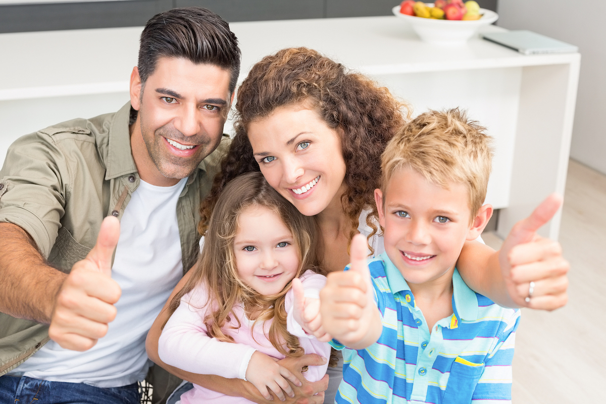 Happy parents giving thumbs up with their young children at home in kitchen